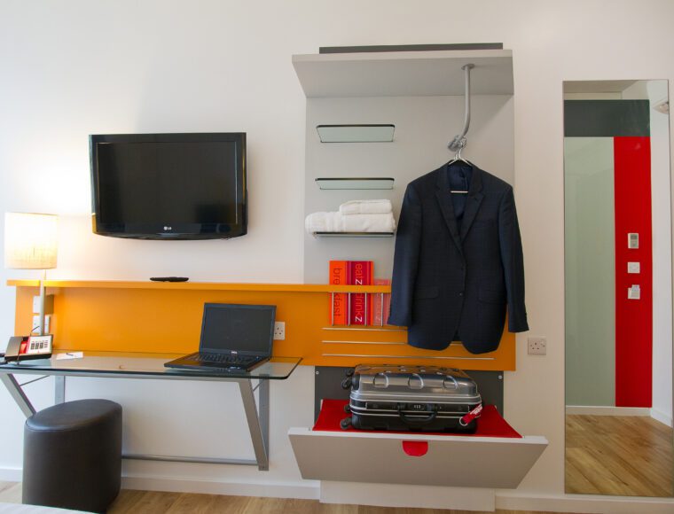 Double room with a work station, television and shelves with a suitcase on it.