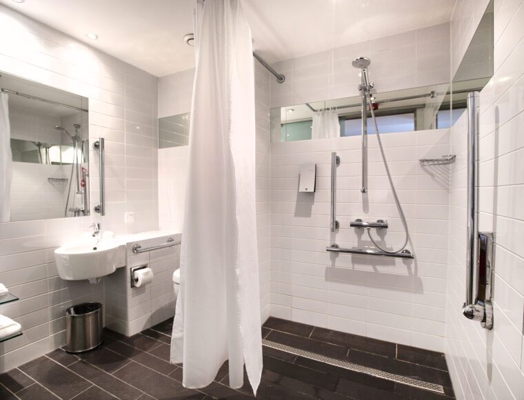 Large bathroom with an accessible shower, toilet, sink and shelves.